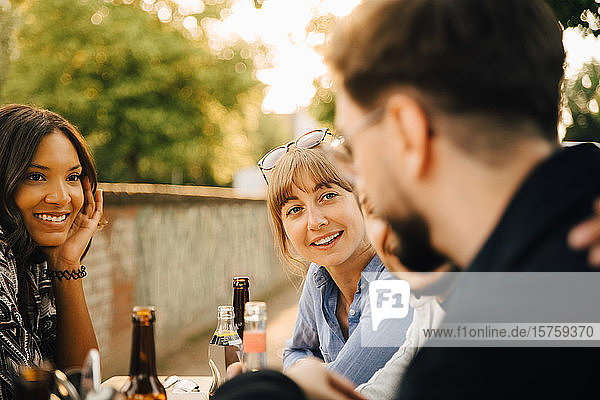 Lächelnde Frauen sitzen neben männlichen Freunden auf Gartenparty