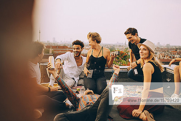 Glückliche Frau spielt Musik über Lautsprecher  während sie mit Freunden auf einer Dachparty genießt