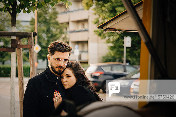 Man embracing sad woman while standing in city
