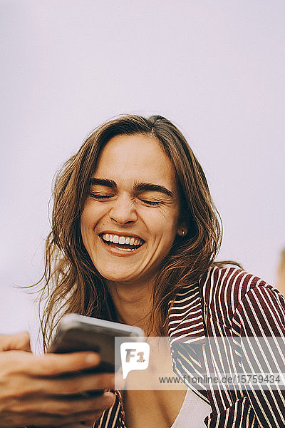Fröhliche junge Frau betrachtet Smartphone  das von einem Freund auf der Terrasse gehalten wird