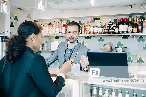Owner looking at businesswoman doing contactless payment in office cafe