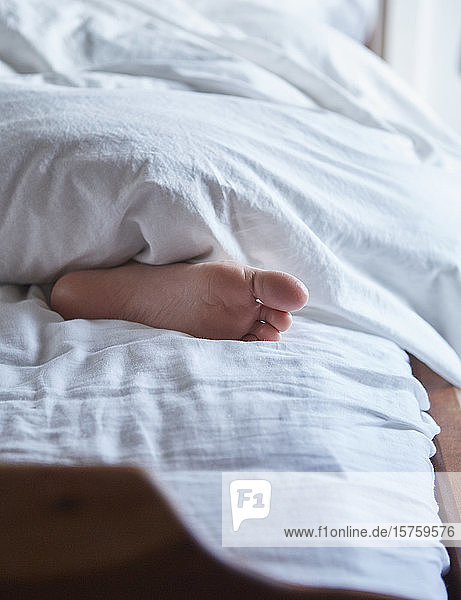 Fuß unter der Bettdecke im Bett