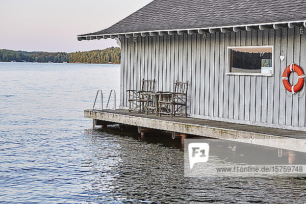 Eine über dem Wasser eines Sees gebaute Hütte am Wasser  Stühle aus Baumzweigen auf der Veranda