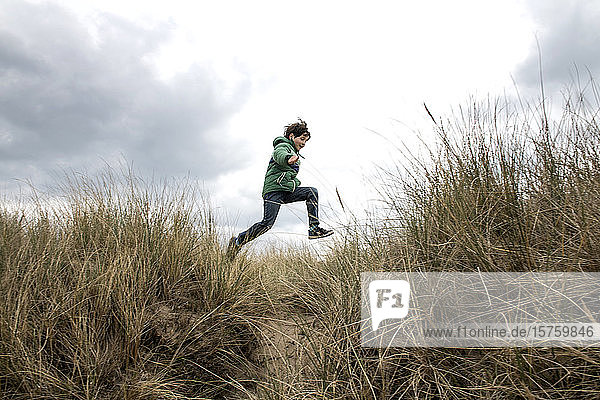 Boy jumping over dry grass on beach