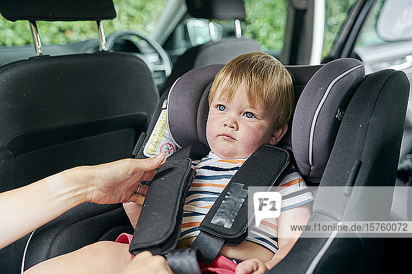 Toddler being strapped into a child car seat in the back of a family car.