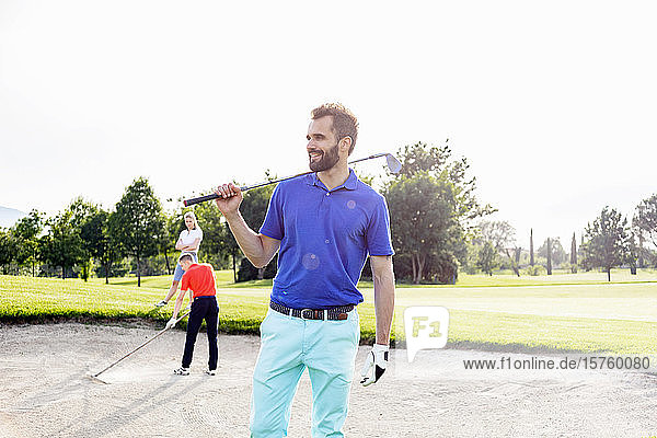 Mann mit Golfschläger auf dem Golfplatz  Freunde spielen Golf im Hintergrund
