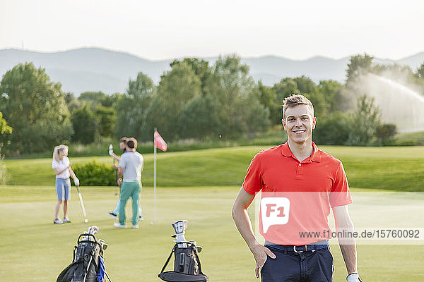 Mann mit Freunden beim Golfspielen auf dem Golfplatz im Hintergrund