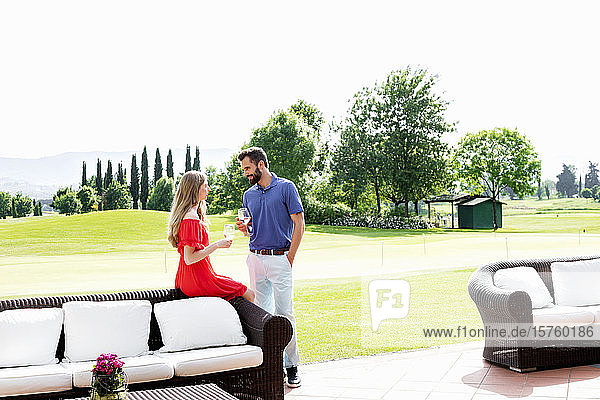 Paar mit Weingläsern unterhält sich neben dem Sofa auf dem Golfplatz