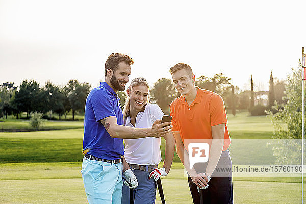 Freunde lesen Textnachricht im Smartphone auf dem Golfplatz