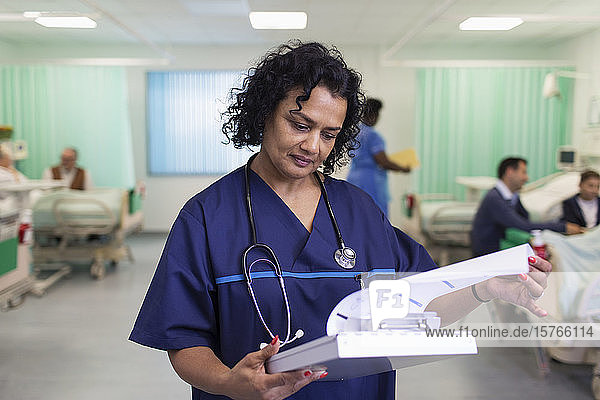 Focused female doctor making rounds  looking at medical chart in hospital ward