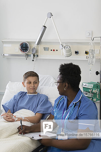 Krankenschwester mit Klemmbrett im Gespräch mit einem jungen Patienten im Krankenhauszimmer