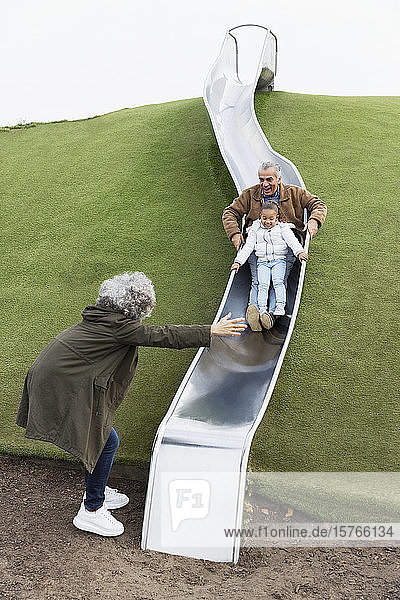 Großeltern mit Enkelin auf Spielplatzrutsche