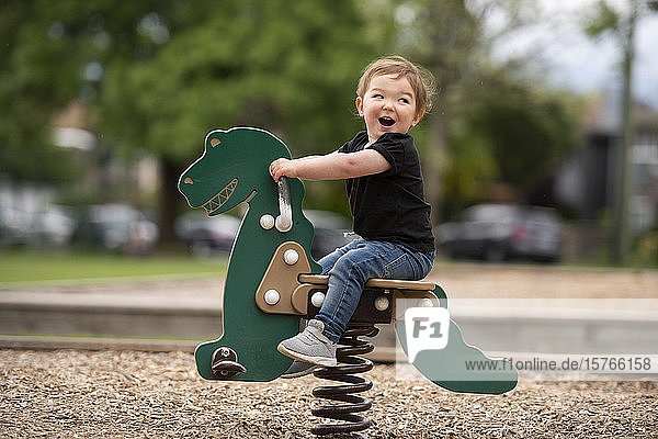 Carefree cute toddler girl riding dinosaur toy at playground