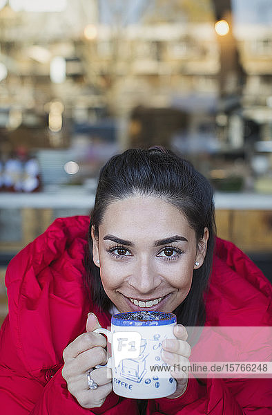 Porträt einer lächelnden  selbstbewussten jungen Frau  die im Fenster eines Cafés Kaffee trinkt