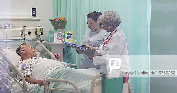 Ärzte mit Krankenblatt machen Visite  sprechen mit älterem Patienten im Krankenhauszimmer