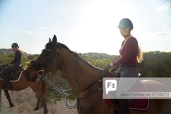 Portrait happy young woman horseback riding on sunny beach