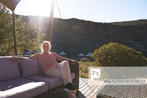 Sorglose ältere Frau entspannt sich auf dem sonnigen Balkon einer Safari-Lodge