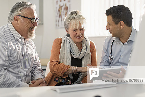 Arzt mit digitalem Tablet trifft sich mit Paar in Arztpraxis