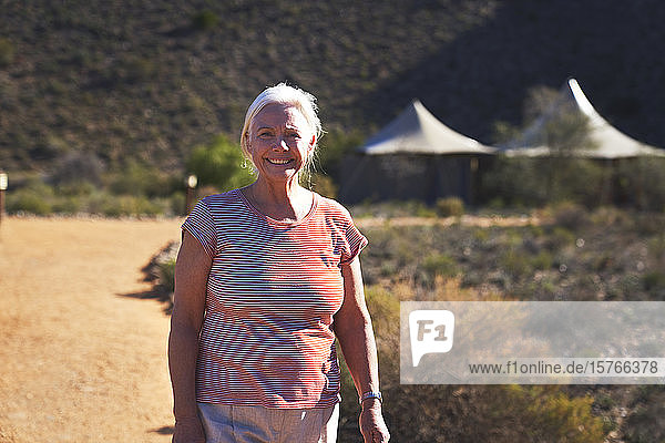 Porträt glückliche ältere Frau auf sonnigem Fußweg vor Safari-Lodge