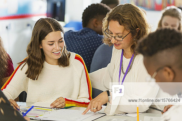 Female high school teacher helping girl student with homework in classroom