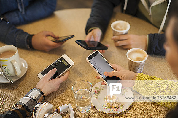 Freunde junger Erwachsener benutzen Smartphones und trinken Kaffee in einem Café
