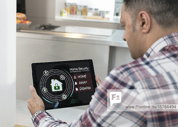 Mann stellt über ein digitales Tablet in der Küche einen intelligenten Hausalarm ein