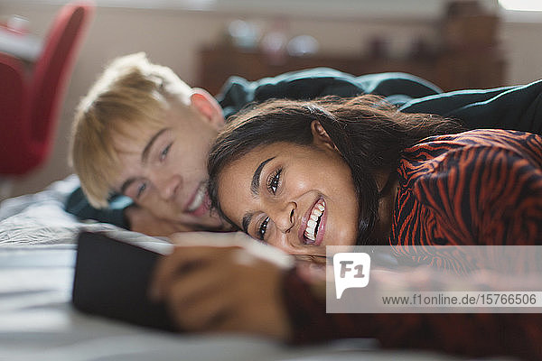 Lächelndes Teenager-Paar mit Smartphone auf dem Bett