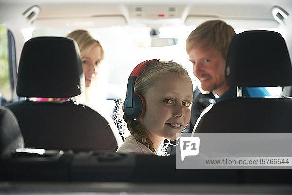 Portrait lächelndes Mädchen mit Kopfhörern auf dem Rücksitz eines Autos