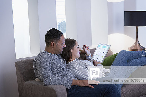 Paar entspannt sich auf dem Wohnzimmersofa und benutzt ein digitales Tablet
