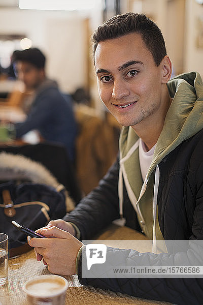 Porträt eines selbstbewussten jungen Mannes  der ein Smartphone in einem Café benutzt