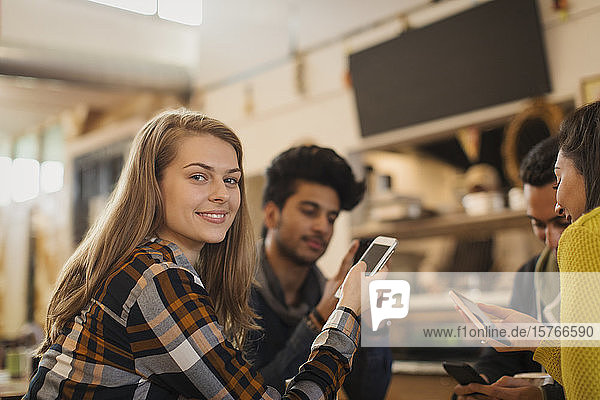 Porträt einer selbstbewussten jungen Frau  die in einem Café mit Freunden ein Smartphone benutzt