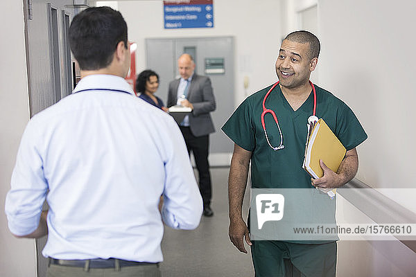 Lächelnder männlicher Chirurg  der einen vorbeigehenden Arzt im Krankenhausflur begrüßt