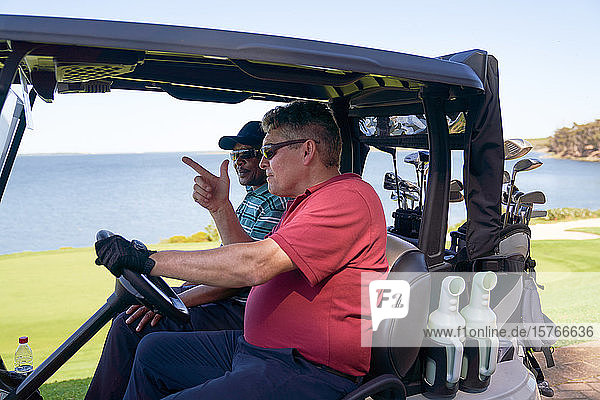Männliche Golfer fahren Golfwagen auf einem Golfplatz am See