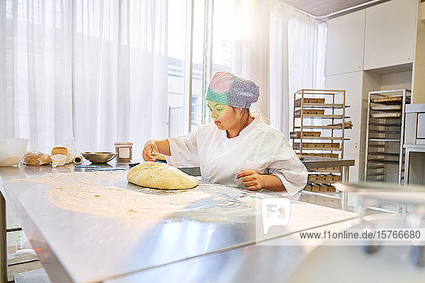 Young woman with Down Syndrome preparing bread dough in kitchen