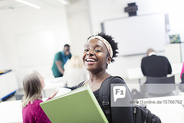 Porträt einer glücklichen  selbstbewussten Studentin mit Mappe im Klassenzimmer