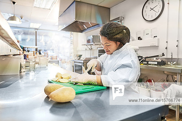 Junge Frau mit Down-Syndrom schneidet Kartoffeln in der Küche eines Cafés