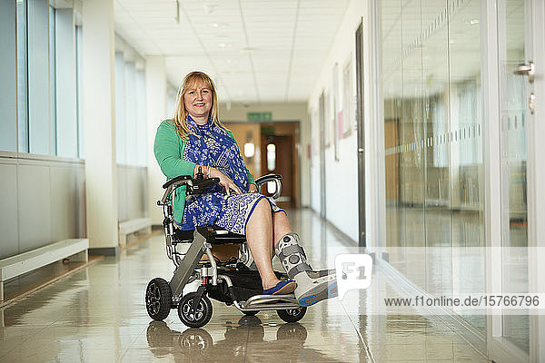 Porträt einer lächelnden Frau mit medizinischem Schuh in einem Rollstuhl auf einem Korridor