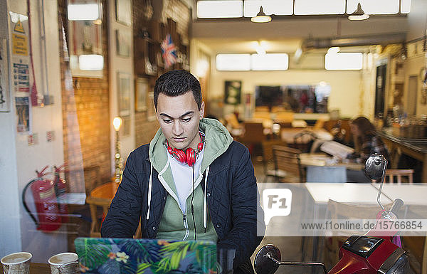 Focused young male college student studying at laptop in cafe window