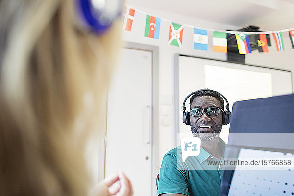 Älterer männlicher Student einer Volkshochschule mit Kopfhörern am Computer im Klassenzimmer