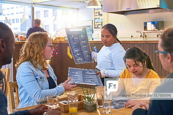 Junge weibliche Bedienung mit Down-Syndrom  die den Kunden in einem Café die Speisekarte gibt