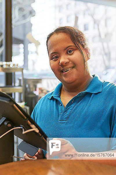 Porträt einer selbstbewussten jungen Frau mit Down-Syndrom  die in einem Café arbeitet