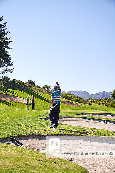 Glücklicher Mann beim Golfen  der auf einem sonnigen Golfplatz jubelt