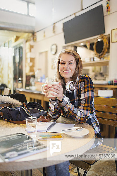 Portrait confident young female college student drinking coffee and studying in cafe