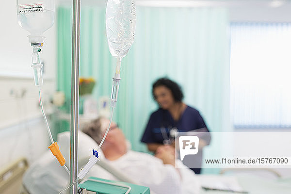 Arzt spricht mit Patientin hinter IV-Tropfen im Krankenhauszimmer