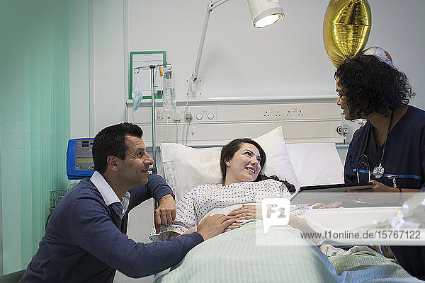 Doctor with digital tablet making rounds  talking with couple in hospital room