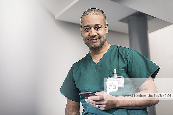Porträt eines selbstbewussten  lächelnden männlichen Chirurgen  der ein Smartphone benutzt