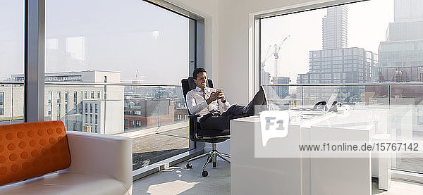 Geschäftsmann mit hochgelegten Füßen auf dem Schreibtisch in einem sonnigen  modernen  städtischen Büro