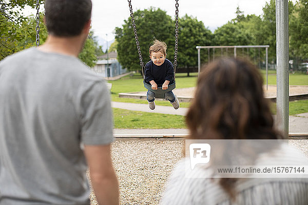 Eltern beobachten sorgloses Kleinkindmädchen beim Schaukeln auf dem Spielplatz