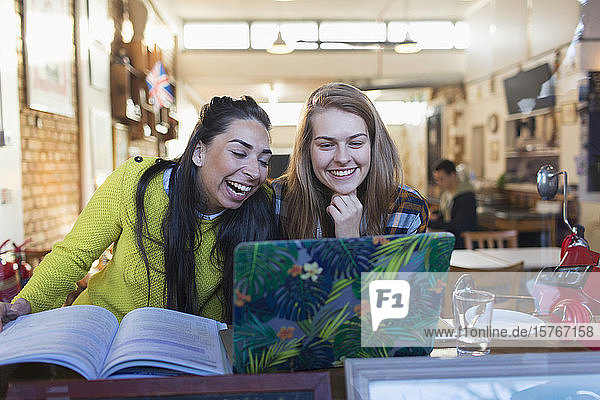 Fröhliche  lachende junge Studentinnen mit Laptop in einem Caféfenster