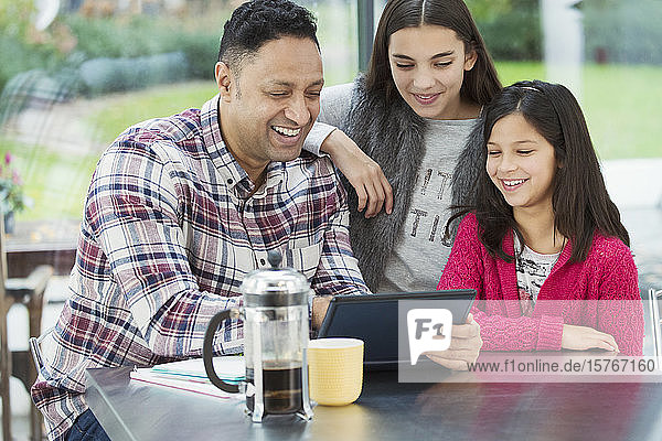 Ein glücklicher Vater und seine Töchter benutzen ein digitales Tablet in der morgendlichen Küche